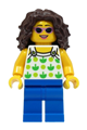 Female beach tourist with dark brown hair wearing a white top with green apples and lime dots, and blue legs - twn462